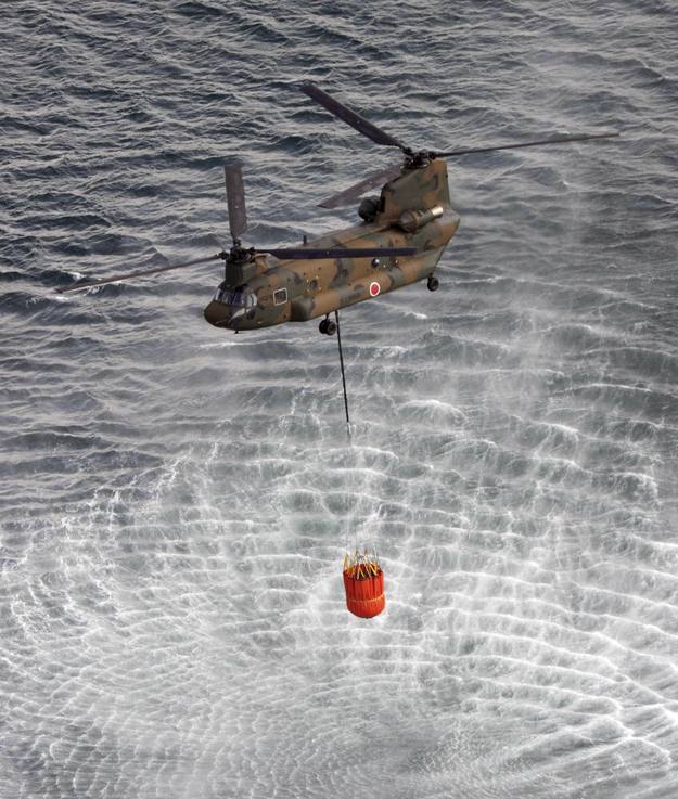Un helicóptero recoge agua en el mar para lanzarla sobre los reactores de la central.